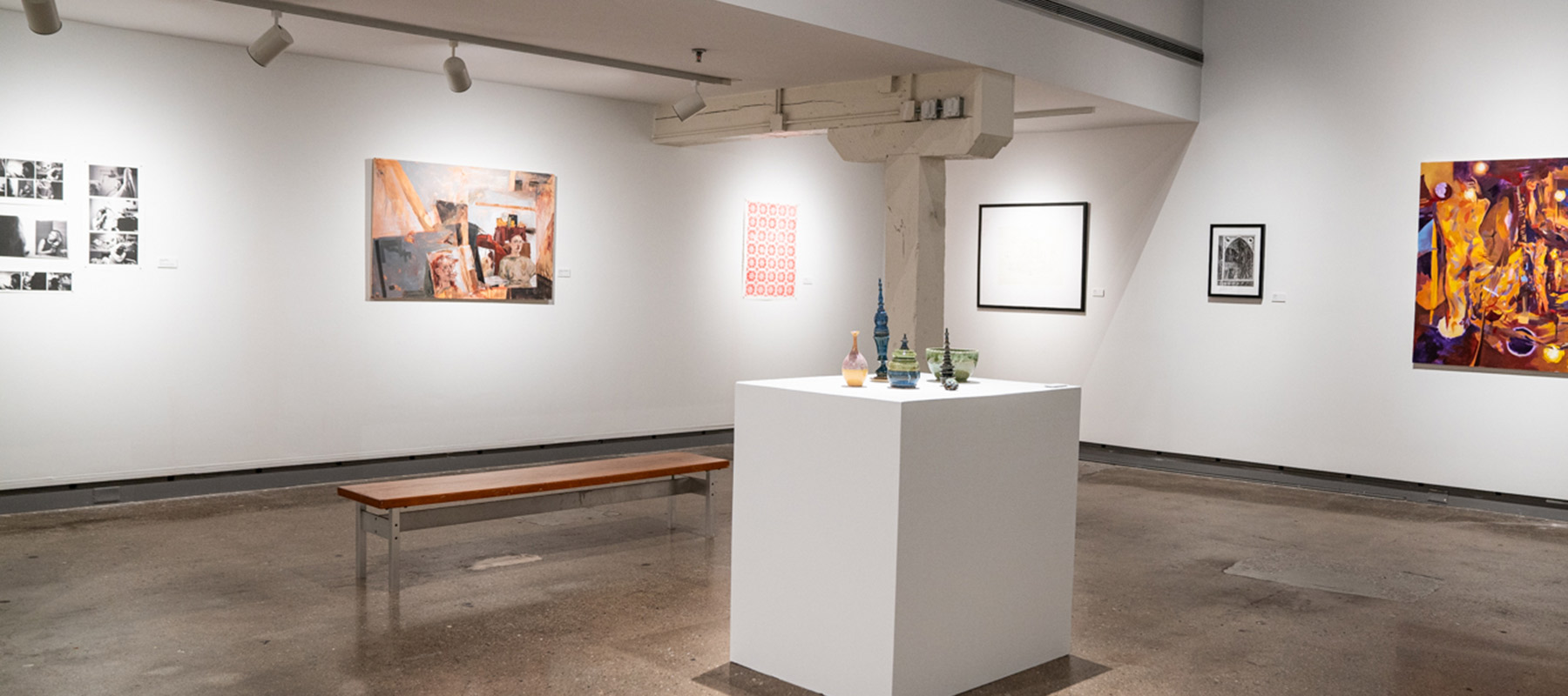 ceramic vessels on a pedestal with artwork on the wall behind them