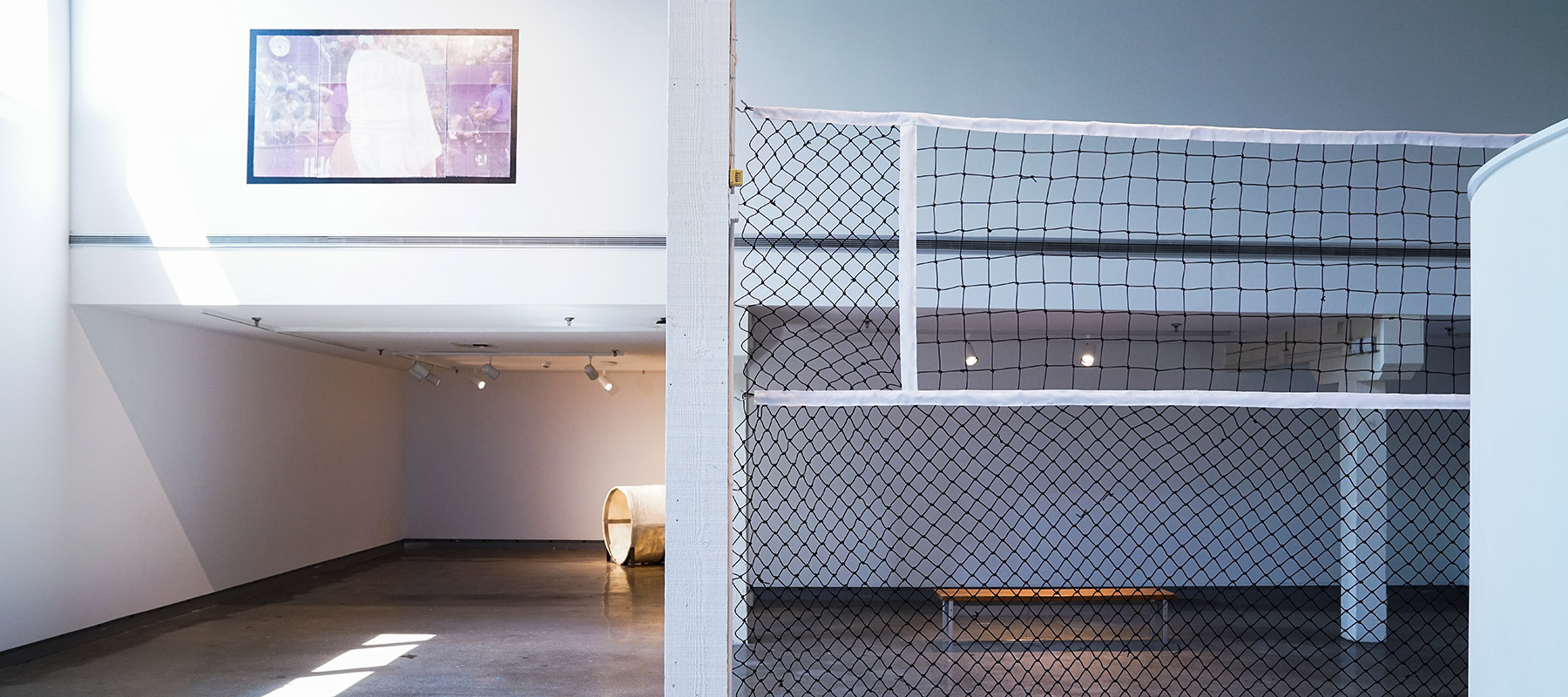 gallery space displaying a large sports net, a large screenprint of a tennis player, and a tunnel made of wool and steel