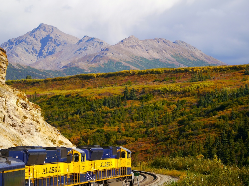Alaskan Railroad with train passing by mountains.